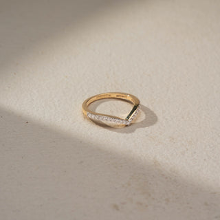 Top view of a curved diamond wedding band in 14 KT Yellow Gold, featuring a chevron-shaped silhouette adorned with pavé-set round lab-grown diamonds, displayed against a beige backdrop.