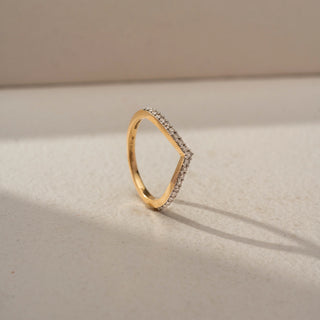 Angled view of a curved diamond wedding band in 14 KT Yellow Gold, featuring a chevron-shaped silhouette adorned with pavé-set round lab-grown diamonds, displayed against a beige backdrop.
