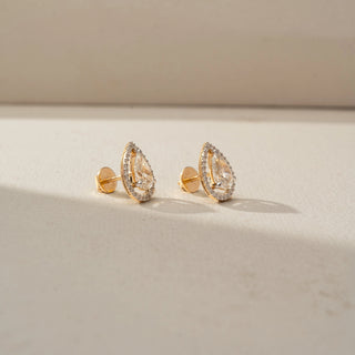 Side view of pear-shaped diamond halo stud earrings in yellow gold, highlighting the elevated setting, pavé halo, and secure post-back design on a neutral backdrop.
