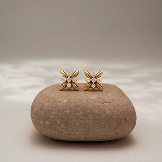 Front view of floral diamond stud earrings in 14 KT Yellow Gold, featuring polished petal motifs with a sparkling round diamond flower cluster at the center, displayed on a textured stone surface.
