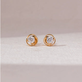 Front view of swirl diamond stud earrings in yellow gold, featuring centred round lab-grown diamonds encased in interlocking circular loops. Placed on a soft beige surface, the design reflects modern elegance.

