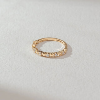 Top view of heart motif diamond band ring in yellow gold, featuring alternating heart shapes and round lab-grown diamonds along the band. Set on a soft neutral surface, it reflects delicate charm and sparkle.