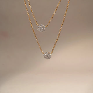 Close Up  view of a floral diamond pendant necklace in 14 KT Yellow Gold, featuring round diamond flower cluster motifs suspended on a delicate double-layer chain against a soft neutral backdrop.
