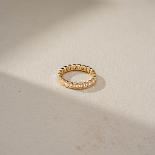 Top view of an emerald-cut diamond eternity band in 14 KT Yellow Gold, featuring bezel-set emerald-cut lab-grown diamonds encircling the entire band in a timeless design, displayed against a beige backdrop.