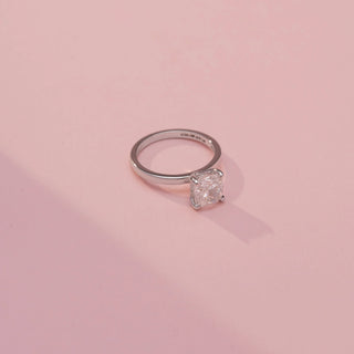 Side view of a cushion-cut solitaire ring in White Gold, featuring a cushion-cut lab-grown diamond in a classic four-prong setting, displayed against a soft pink backdrop.
