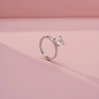Angled view of a cushion-cut solitaire ring in White Gold, featuring a cushion-cut lab-grown diamond in a classic four-prong setting, displayed against a soft pink backdrop.