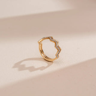 Side view of Reia’s 14 KT Yellow Gold Modern Chevron Band. The architectural zigzag silhouette is shown on a gold band against a soft pink surface, highlighting the parallel polished and diamond rails.