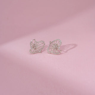 Front view of a 14KT white gold earrings featuring round-cut diamonds in a butterfly-inspired design, set against a pink background.