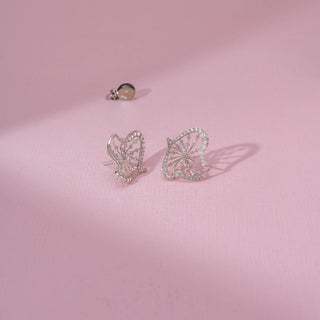 Angled view of a 14KT white gold earrings featuring round-cut diamonds in a butterfly-inspired design, set against a pink background.