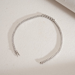 Flat lay view of Constellation Tennis Diamond Bracelet against beige background. Made in 14KT hallmarked white gold with spring lock clasp. Set with EF colour, VVS clarity lab grown diamonds totaling 2.03 carats. Bracelet weighs 5.79 grams, priced INR 50,000–1,00,000.