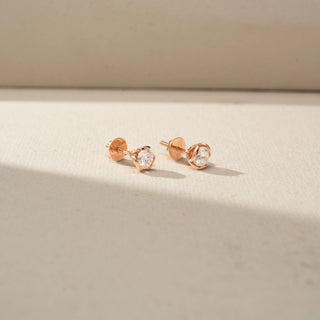 Side view of round diamond stud earrings in rose gold, showcasing the floral-inspired petal setting, elevated profile, and secure post-back design on a neutral backdrop.