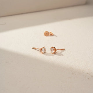 Angled side view of round diamond stud earrings in rose gold, highlighting the floral-inspired petal setting, open gallery design, and secure post backs on a softly lit surface.