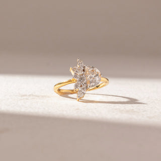 Front view of pear-shaped diamond cluster ring in yellow gold, featuring a central pear diamond with marquise and round accents, set on a soft neutral surface, highlighting a floral-inspired sparkle.
