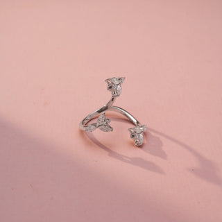 Top view of a floral wrap ring in White Gold, featuring marquise-shaped lab-grown diamond clusters arranged along an open-ended spiral band, displayed against a soft pink backdrop.
