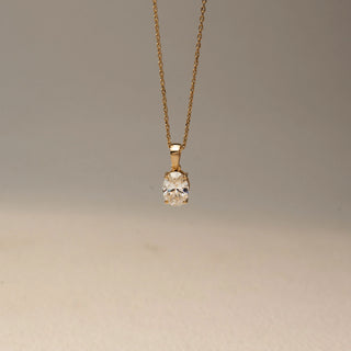 Front view of a solitaire diamond pendant necklace in 14 KT Yellow Gold, featuring an oval-cut diamond suspended from a delicate gold chain against a soft neutral backdrop.