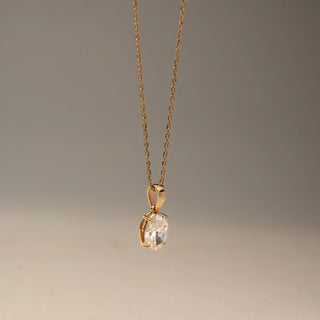 Side view of a solitaire diamond pendant necklace in 14 KT Yellow Gold, featuring an oval-cut diamond suspended from a delicate gold chain against a soft neutral backdrop.