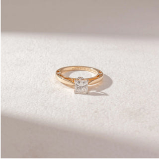 Top view of princess-cut diamond solitaire ring in yellow gold with a split-style band, set on a soft neutral surface, highlighting crisp symmetry and refined, radiant brilliance.
