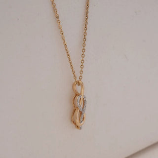 Side view of Infinity Loop Golden Diamond Pendant in yellow gold, highlighting intertwined infinity curves accented with round lab-grown diamonds and a subtle dangling detail against a soft beige backdrop.