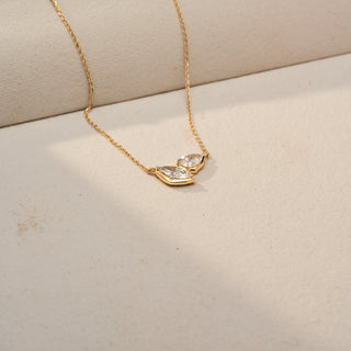 Angled view of a marquise diamond necklace in 14 KT Yellow Gold, featuring two marquise-cut lab-grown diamonds arranged in a graceful V-shaped design, suspended from a delicate chain against a beige backdrop