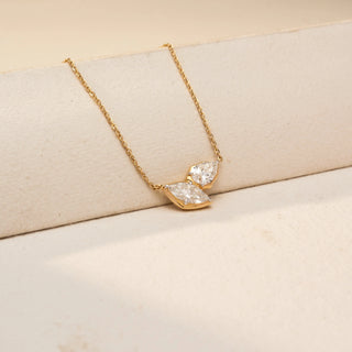 Close Up view of a marquise diamond necklace in 14 KT Yellow Gold, featuring two marquise-cut lab-grown diamonds arranged in a graceful V-shaped design, suspended from a delicate chain against a beige backdrop
