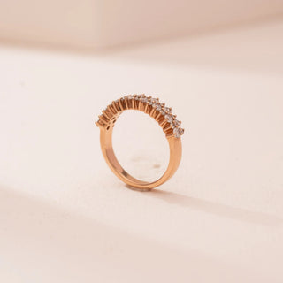 Side view of Reia’s 14 KT Rose Gold Eternal Glow Band. The polished rose gold band, and its elevated row of radiant pavé-set round diamonds, are shown against a soft pink surface.