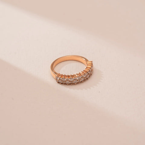 Top view of Reia’s 14 KT Rose Gold Eternal Glow Diamond Band Ring. A continuous row of pavé-set round diamonds creates a radiant glow on a warm gold band against a soft pink surface.