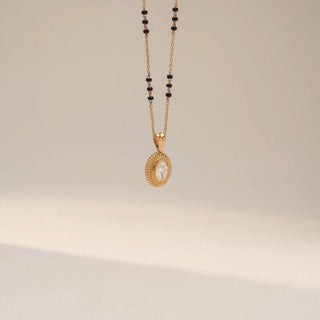 Angled view of a yellow gold lab-grown diamond mangalsutra featuring an oval solitaire diamond pendant with a vintage-inspired textured halo on a delicate black bead chain, displayed on a neutral background.