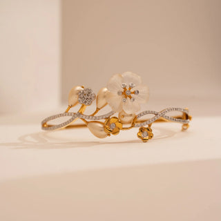 Front view of Reia’s 14 KT Yellow Gold Ornate Pearl Floral Diamond Bracelet. It features a carved shell blossom, lustrous pearls, and diamond-set gold bands on a cream backdrop.