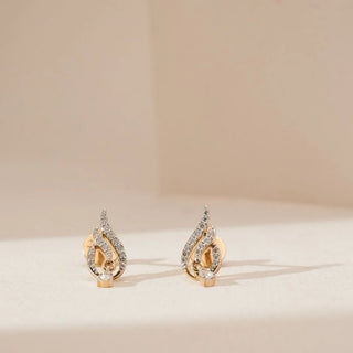 Front view of sweeping droplet diamond stud earrings featuring curved yellow gold strands accented with pavé-set round lab-grown diamonds, displayed on a soft neutral studio surface.
