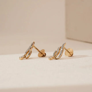 Side angled view of sweeping droplet diamond stud earrings with curved yellow gold design and pavé-set round lab-grown diamonds, highlighting the screw back fastening on a neutral surface.