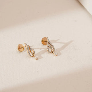 Angled view of sweeping droplet diamond stud earrings featuring curved yellow gold strands with pavé-set round lab-grown diamonds and a delicate teardrop accent, placed on a soft neutral surface.