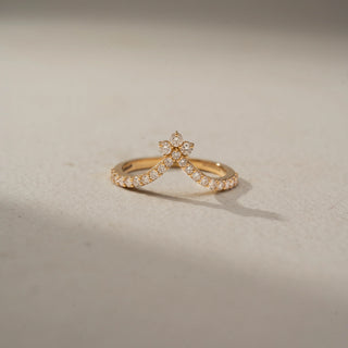 Front view of a floral-inspired diamond ring in 14 KT Yellow Gold, featuring a petite flower cluster atop a V-shaped pavé-set diamond band, displayed against a beige backdrop.
