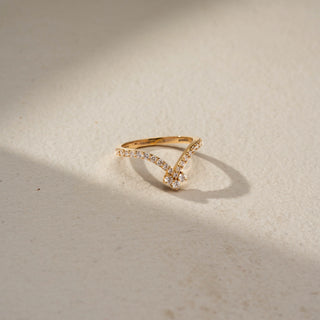 Top view of a floral-inspired diamond ring in 14 KT Yellow Gold, featuring a petite flower cluster atop a V-shaped pavé-set diamond band, displayed against a beige backdrop.