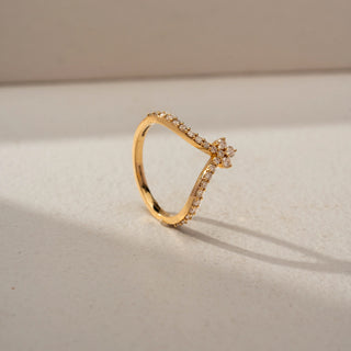 Angled view of a floral-inspired diamond ring in 14 KT Yellow Gold, featuring a petite flower cluster atop a V-shaped pavé-set diamond band, displayed against a beige backdrop.