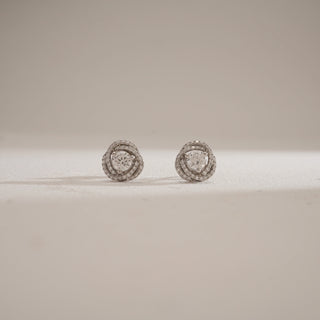 Front view of Cluster Halo Diamond Stud Earrings against beige background. Designed in 14KT hallmarked white gold, secured with bombay screw closure. Adorned with EF colour, VVS clarity lab grown diamonds totaling 1.42 carats, including a 0.47-carat solitaire. Weighs 3.43 grams, priced INR 50,000–1,00,000.