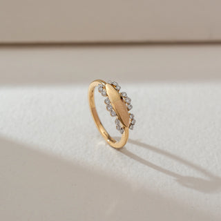 Side angled view of oval halo diamond ring in yellow gold, featuring an elongated oval centre plate bordered by round lab-grown diamonds along the edges. Set on a soft neutral backdrop, it highlights sleek form and subtle sparkle.
