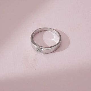 Top angled view of an elegant minimalist radiant diamond ring in white gold, showcasing a single round lab-grown diamond set within a smooth flat band, placed on a soft pink surface.