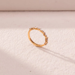Side view of multi-shape diamond band in yellow gold, featuring alternating baguette and round lab-grown diamonds along a curved setting. Set on a textured beige surface, the design casts a soft shadow.