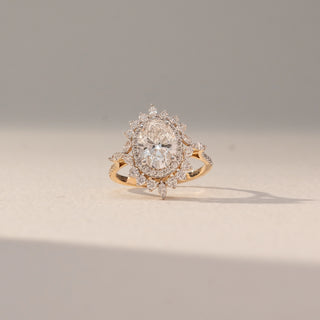 Front view of Vintage Halo Diamond Ring in 14KT Yellow Gold, featuring an oval lab grown diamond encircled by a halo with marquise accents. Set on a beige backdrop, the design highlights ornate brilliance and elegance.
