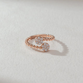 Top view of open bead diamond ring in rose gold, featuring two circular cluster heads set with round lab-grown diamonds on a beaded band. Set on a soft neutral surface, it reflects playful elegance and sparkle.