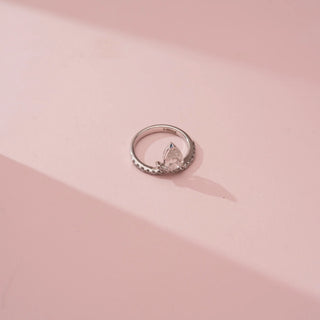 Top-down view of Reia’s 14 KT White Gold Pear Grace Diamond Wrap Ring. Captured on a pink backdrop, it highlights the intricate pavé settings and the brilliance of the pear diamond.
