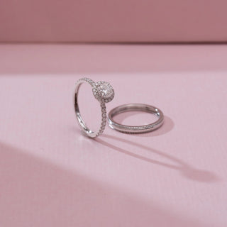 Angled view of Timeless Pavé Accented Diamond Ring in white gold, featuring a round lab-grown diamond with halo detailing and a pavé-set band, displayed beside a matching band on a soft pink backdrop.