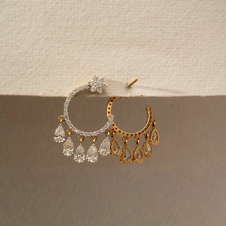 Angled view of diamond hoop earrings featuring floral cluster tops, pavé-set hoops, and dangling pear-shaped diamonds, showing both front and back details on a cream backdrop.
