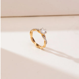 Angled view of Braided Twisted Solitaire Diamond Ring in yellow gold, featuring a round lab-grown diamond set on an intertwined twisted band with diamond accents, displayed on a soft beige backdrop.