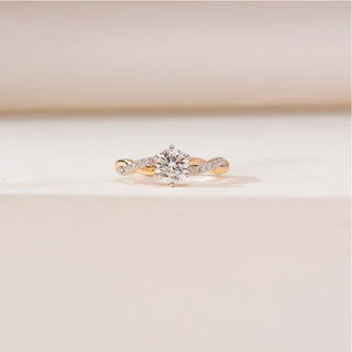Front view of Braided Twisted Solitaire Diamond Ring in yellow gold, featuring a round lab-grown diamond set on a gently twisted band with diamond accents, displayed on a soft beige surface.