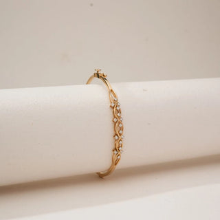 Side view of yellow gold infinity wave diamond bracelet featuring interwoven loops set with round lab-grown diamonds, gracefully wrapped over a neutral display cushion.