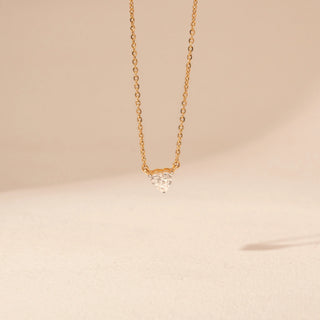 Front view of a 14KT yellow gold necklace featuring a heart-cut diamond pendant, set against a beige background.