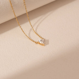 Angled view of a 14KT yellow gold necklace featuring a heart-cut diamond pendant, set against a beige background.