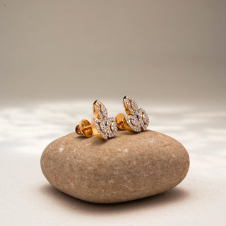 Side view of leaf-inspired diamond stud earrings in 14 KT Yellow Gold, featuring marquise-shaped open motifs outlined with pavé-set diamonds, displayed on a textured stone surface.