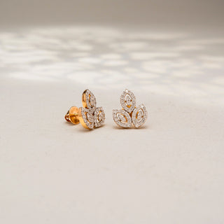 Angled view of leaf-inspired diamond stud earrings in 14 KT Yellow Gold, featuring marquise-shaped open motifs outlined with pavé-set diamonds, displayed on a textured stone surface.
